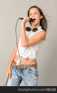 Singing teenage girl with microphone closed eyes on gray background