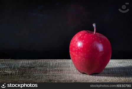 Single apple on a wooden table. Blurred dark background.