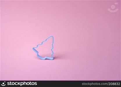 Single blue cookies cutter in shape of a Christmas tree, on a pink background. Xmas baking concept. Minimalist culinary image.