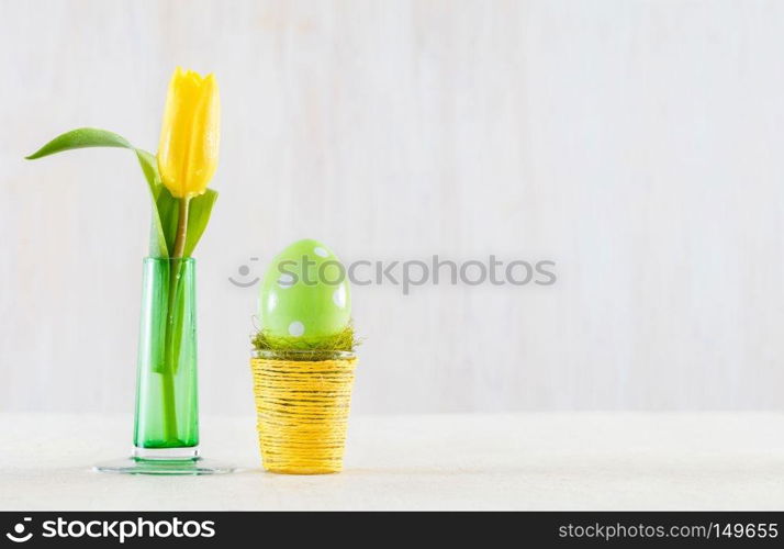 Single easter handmade egg in a pot on wooden table. Fresh tulip in a glass vase.. Single easter egg in a pot.