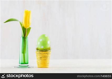 Single easter handmade egg in a pot on wooden table. Fresh tulip in a glass vase.. Single easter egg in a pot.