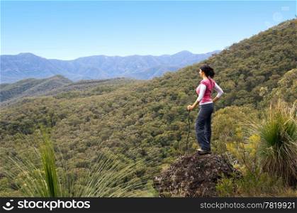 Single female hiker looks out at view in mountains with forest below her