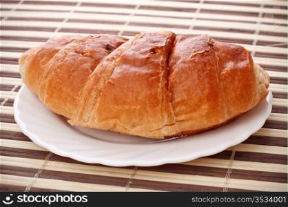 single fresh croissant laying on white dish