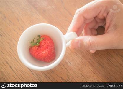 Single fresh ripe strawberry in white mug, stock photo