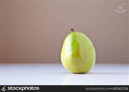 Single green pear on white table with taupe brown background. The concepts depicted in this image are nutrition, good food choices, balanced diet and good for you.