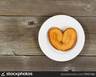 Single heart shaped cookie on white plate with rustic wood in background.