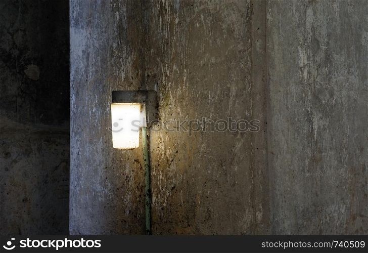 Single lamp shining on dark dirty concrete wall.