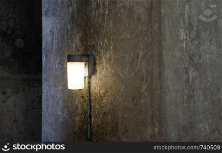 Single lamp shining on dark dirty concrete wall.