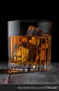 Single malt scotch whiskey in crystal glass with ice cubes on wooden table background. Macro