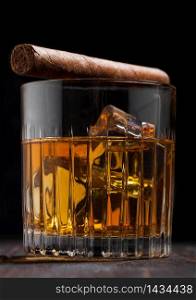 Single malt scotch whiskey in crystal glasses with ice cubes and cuban cigar on wooden table background. Macro