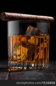 Single malt scotch whiskey in crystal glasses with ice cubes and cuban cigar on wooden table background. Macro