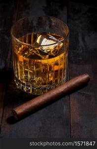 Single malt scotch whiskey in crystal glasses with ice cubes and cuban cigar on wooden table background.