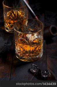 Single malt scotch whiskey in crystal glasses with ice cubes and smoking pipe on wooden table background. Top view