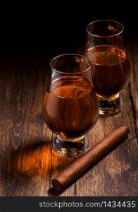 Single malt scotch whiskey in glencairn glasses with cuban cigar on wooden table background. Top view