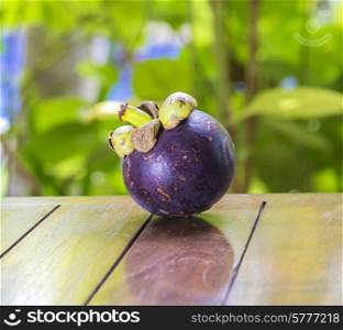 Single Mangostin and Fresh Green Leaf on Wooden Table