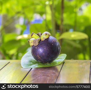 Single Mangostin and Fresh Green Leaf on Wooden Table