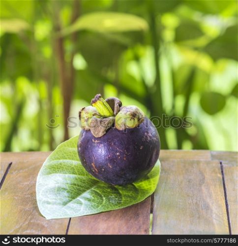 Single Mangostinon and Fresh Green Leaf on Wooden Table