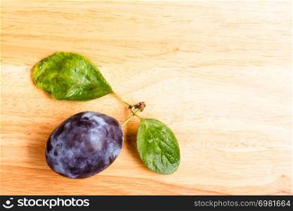 Single prune plum fruit with green leaves on wooden table copy space text area