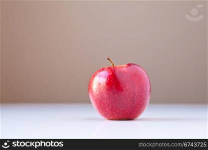 Single red apple on white table with taupe brown background. The concepts depicted in this image are nutrition, good food choices, balanced diet and good for you.