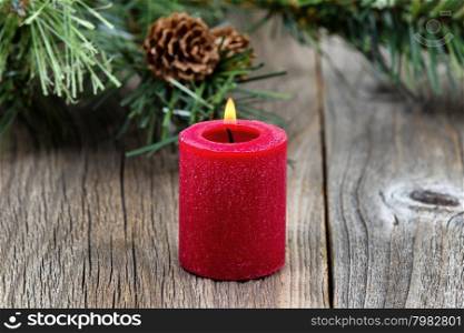 Single red candle with flame and evergreen setting on rustic wood. Selective focus on front part of candle and flame.