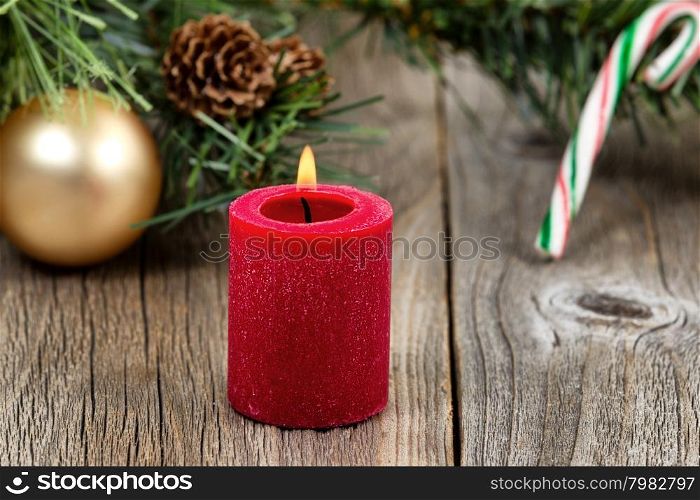 Single red candle with flame and ornaments in evergreen setting on rustic wood. Selective focus on front part of candle and flame.