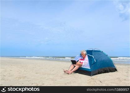 Single senior man with digital tablet camping in shelter at the beach