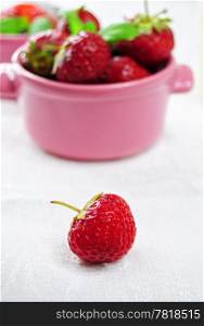 Single strawberry on white table, cup with more fruit on the background