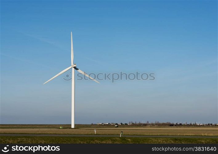 single white windmill with very blue summer sky and green farmland with farm on the background and street with cars in front