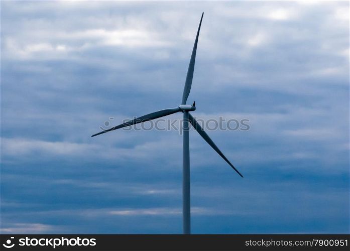 Single wind turbine tower and propeller on dark cloudy sky.