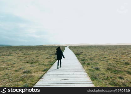 Single woman walking an endless wooden path to the dunes