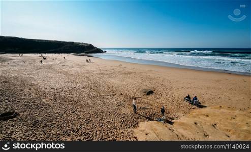 Sintra, Portugal - Jan 5, 2020: Families enjoy a relaxing afternoon at the golden Praia das Macas in Portugal on a sunny winter day. Families enjoy a relaxing afternoon at the golden Praia das Macas in Portugal on a sunny winter day