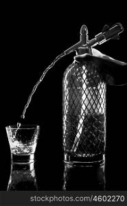 siphon with soda copulation on the table on a black background with a full glass, jet and drops
