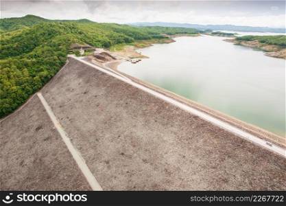 Sirikit Dam from above. The Sirikit Dam is an embankment dam on the Nan River. Lake, forest and cloudy background. Nan Province, Thailand. Rainy season. Soft sunlight.
