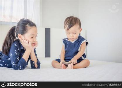 Sister and baby brother using smartphone, watching cartoons together on the bed, happy family and kids playing concept