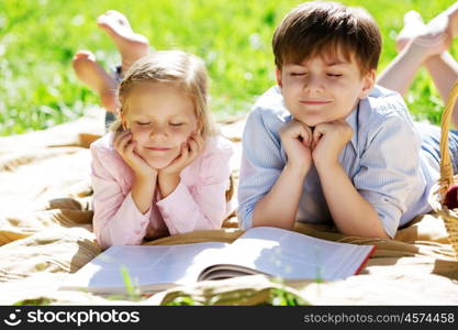 Sister and brother in the park reading a book. Summer weekend outdoors