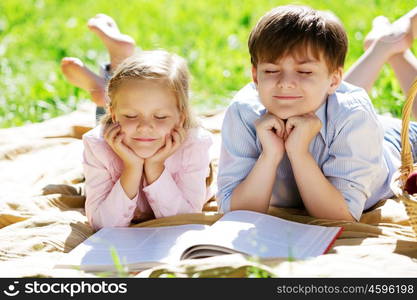 Sister and brother in the park reading a book. Summer weekend outdoors