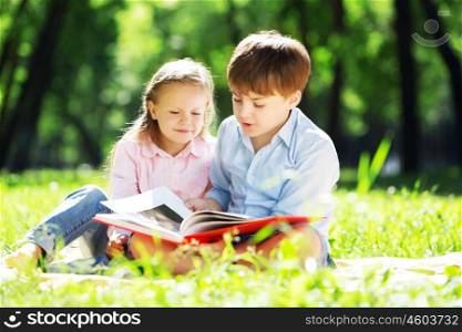 Sister and brother in the park reading a book. Summer weekend outdoors