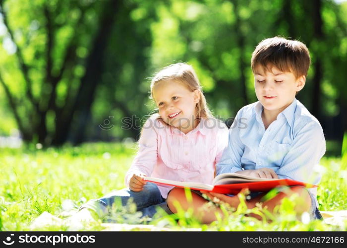 Sister and brother in the park reading a book. Summer weekend outdoors