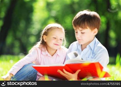Sister and brother in the park reading a book. Summer weekend outdoors