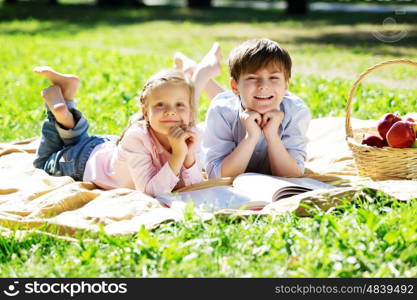 Sister and brother in the park reading a book. Summer weekend outdoors