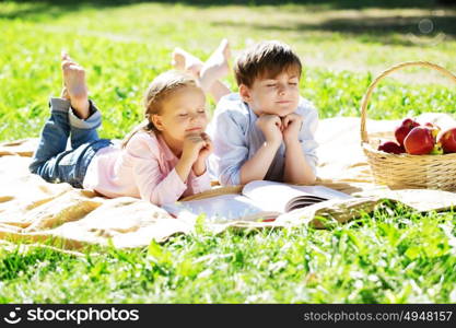 Sister and brother in the park reading a book. Summer weekend outdoors