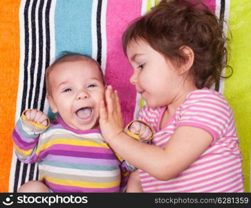 sister and brother lie on a striped towel