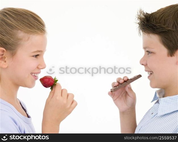 Sister eating strawberry by brother eating chocolate bar