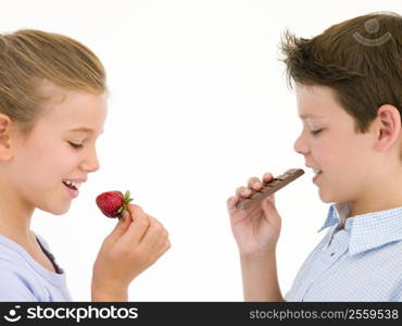 Sister eating strawberry by brother eating chocolate bar