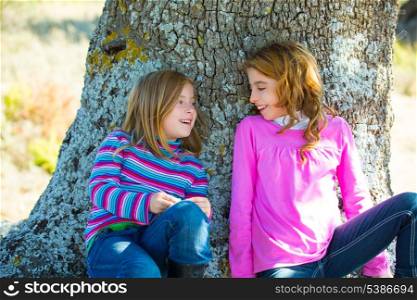 Sister kid girls smiling sit relaxed in a oak tree trunk with jeans