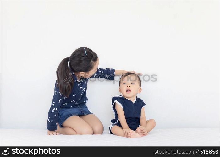 Sister measures the growth of her brother, kids playing on the bed, happy family concept