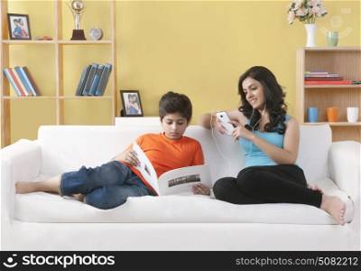 Sister sitting on couch listening to music while little her brother reading book