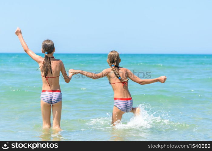 Sisters joyfully and happily run into the sea on a hot sunny day