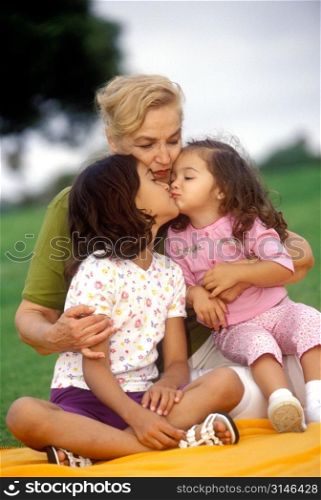Sisters Kissing On A Blanket In The Park With Their Mother