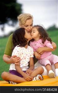 Sisters Kissing On A Blanket In The Park With Their Mother